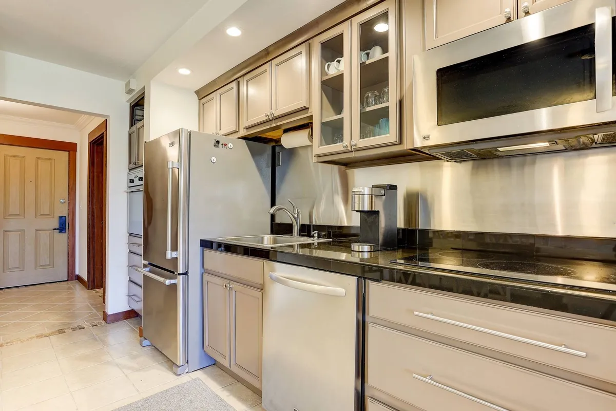 A modern kitchen featuring stainless steel appliances, a sleek black granite countertop, and glass-front cabinets. Bright and functional, the space is ideal for preparing meals and hosting guests, with ample lighting and a welcoming atmosphere.