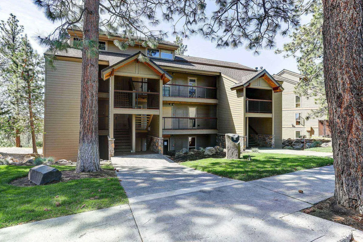 An exterior view of the condo building facade, with a staircase leading to the entryway surrounded by natural landscaping. The scene suggests a welcoming environment with opportunities for outdoor gatherings and relaxation, while also showing the building's ground-level access.