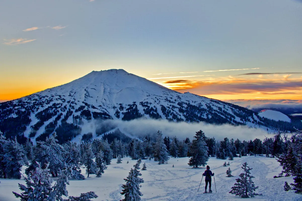 A snow-covered mountain under a glowing sunset sky, accented by a skier in motion among evergreen trees. The scene conveys both the excitement of winter sports and the serene beauty of alpine landscapes.